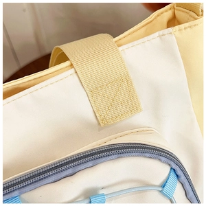 Detail of cross-stitch reinforcement on contrast canvas bag with zipper and nylon strap