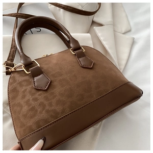 Detail of brown textured shell handbag showing smooth leather trim and metal hardware