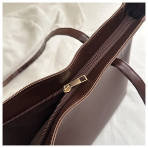 Detail shot of the gold metal zipper and smooth dark brown leather on this large tote bag