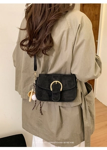Close-up of black matte crossbody bag with gold D-buckle and baseball charm detail