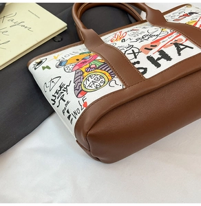 Close-up of graffiti canvas bucket bag with brown leather trim and metal rivets