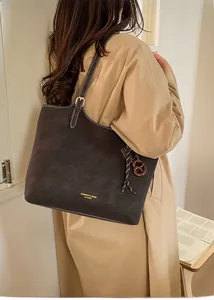 Detail of dark brown tote bag with contrast stitching and woven charm on shoulder