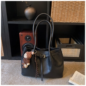 Nahaufnahme der schwarzen Tote Bag aus Leder mit Zierschnalle und braunem Strickbären-Anhänger