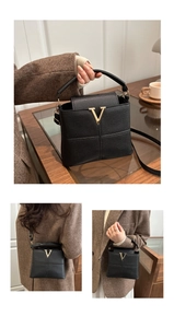 Detail einer schwarzen Lederbeuteltasche mit auffälligem goldenem V-förmigem Metallverschluss