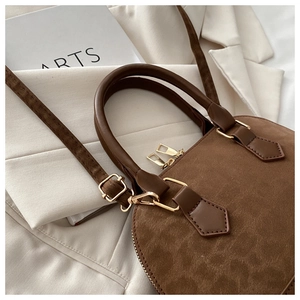 Close-up of brown suede shell bag featuring gold zippers and premium matte texture