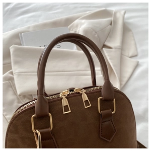 Close-up of matte suede texture and gold zipper detail on the brown shell bag