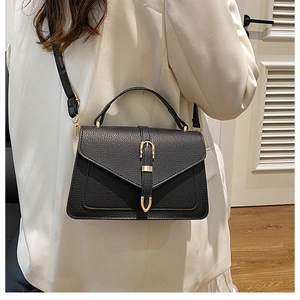 Detailed view of black litchi pattern leather crossbody bag with golden buckle on white suit