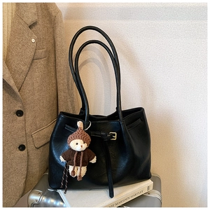 Detail der schwarzen Shopper-Tasche mit Gold-Schnalle und Bär-Anhänger auf Koffer