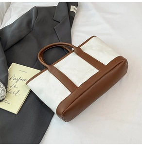 Detail of canvas tote bag with brown leather handles and reinforced bottom panel