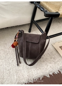 Detail of dark brown retro bucket bag with white contrast stitching and tassel charm