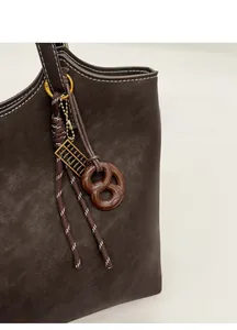 Détail d'un sac cabas en cuir marron avec coutures blanches et breloques fantaisie