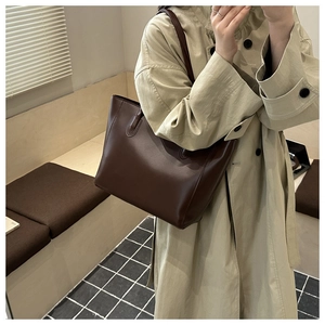 Detail view of a vintage dark brown leather tote bag worn by a model in casual attire