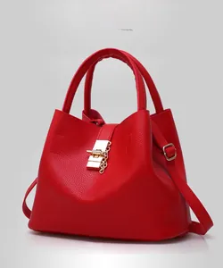 Detail of red pebbled leather handbag with gold twist lock and metal chain decoration