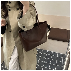 Classic dark brown leather tote bag worn on shoulder in a minimalist indoor setting