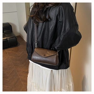 Detailed view of a brown leather accordion crossbody bag worn over a black jacket