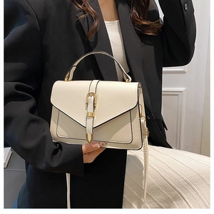 Detail of cream pebbled leather handbag featuring gold belt buckle and top handle