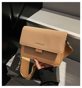 Detail of a brown flap crossbody bag with wide woven strap and fashion branding