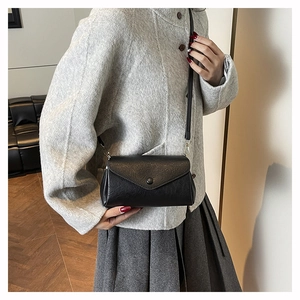Detail of minimalist black leather crossbody bag featuring a magnetic flap closure