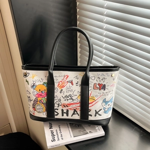 Sac fourre-tout graffiti en toile beige avec anses en cuir noir posé sur un livre