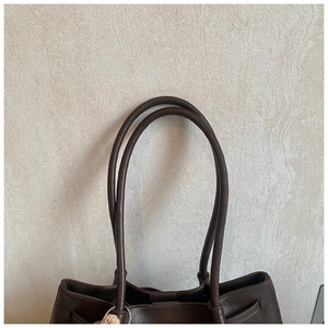 Detailaufnahme der braunen Ledertasche mit Kordelzug, Metallring und Plüsch-Anhänger