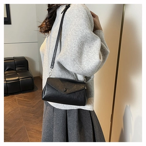 Detail of minimalist black crossbody bag with lychee texture and envelope flap closure