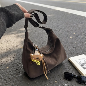 Deep brown crescent tote bag with teddy bear charm shown against a street background