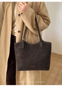 Detail of dark matte leather tote bag featuring contrast stitching and golden buckles