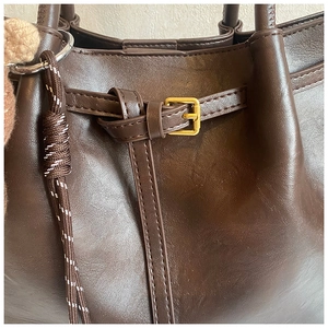 Detail der dunkelbraunen Ledertasche mit goldener Schnalle und gewebtem Kordel-Anhänger