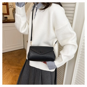 Minimalist black leather crossbody bag with envelope flap shown on model with white knitwear