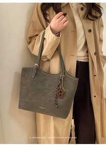 Detail of olive green leather tote bag with gold lettering and decorative pendants
