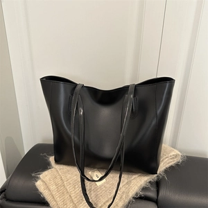 Classic black leather tote bag with dual shoulder straps on a beige knitted background