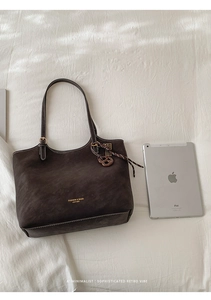 Close-up of dark brown suede tote bag featuring gold hardware and fashion logo details