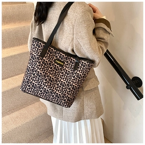 Detail of large leopard print tote bag featuring black leather handles and fashion patch
