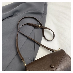 Detail of dark brown retro crossbody bag featuring a golden buckle and fine leather strap