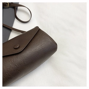 Detail of dark brown leather crossbody bag with lychee texture and adjustable strap