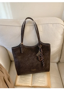 Détail du sac cabas en daim marron avec surpiqûres blanches et pendentif créatif