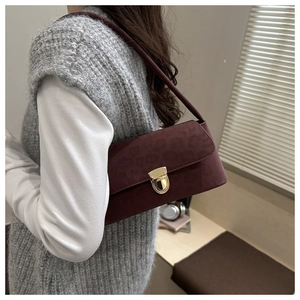 Detail of dark burgundy suede shoulder bag with golden round buckle and matte leather texture