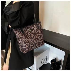 Close-up of leopard print tote bag with gold fashion plaque and black faux leather straps