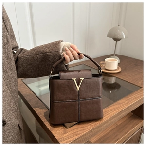 Detail einer Lederhandtasche mit Lychee-Muster und markantem goldener V-förmiger Metall-Logo