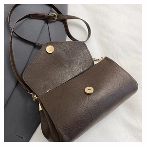Detail of dark brown leather crossbody bag with round golden magnetic buckle and strap