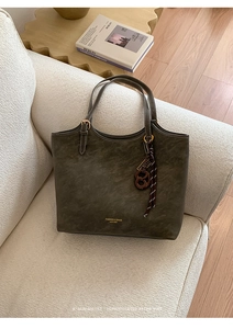 Détail d'un grand sac cabas en daim vert olive avec détails dorés sur un canapé