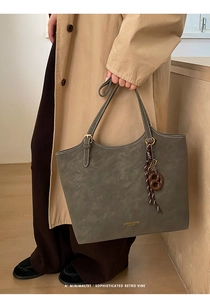 Detail of gray matte leather tote bag with gold hardware and pretzel charm accessory
