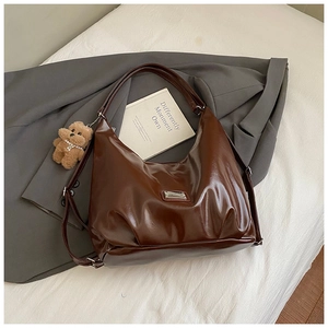 Detail of dark brown glossy leather tote bag featuring a metal logo and plush bear charm