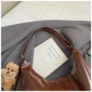 Detailed view of a brown glossy hobo bag with a plush bear charm on a grey blazer