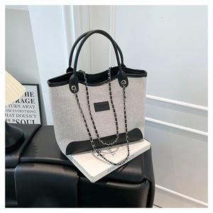 Detail of canvas tote bag with black leather trim, chain strap, and logo patch on white books