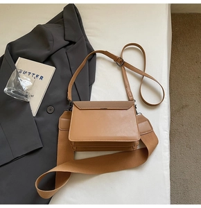 Detail of khaki square crossbody bag with dual straps on a minimalist bed setting