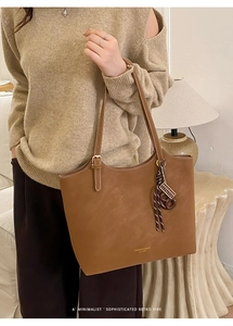 Detail of caramel faux suede tote bag with metallic logo and braided decorative pendant
