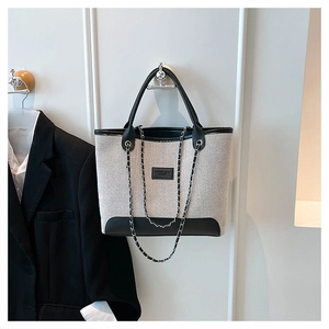 Detail of canvas tote bag featuring contrast leather trim and decorative metal chain