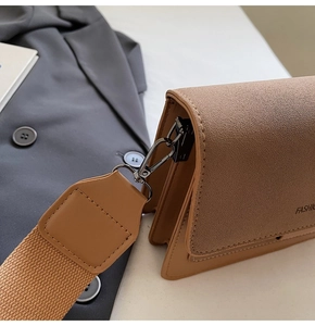 Detail of tan pebble leather shoulder bag showing wide strap and accordion structure