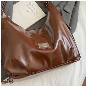 Detail of a brown polished hobo shoulder bag placed on a grey blazer with book